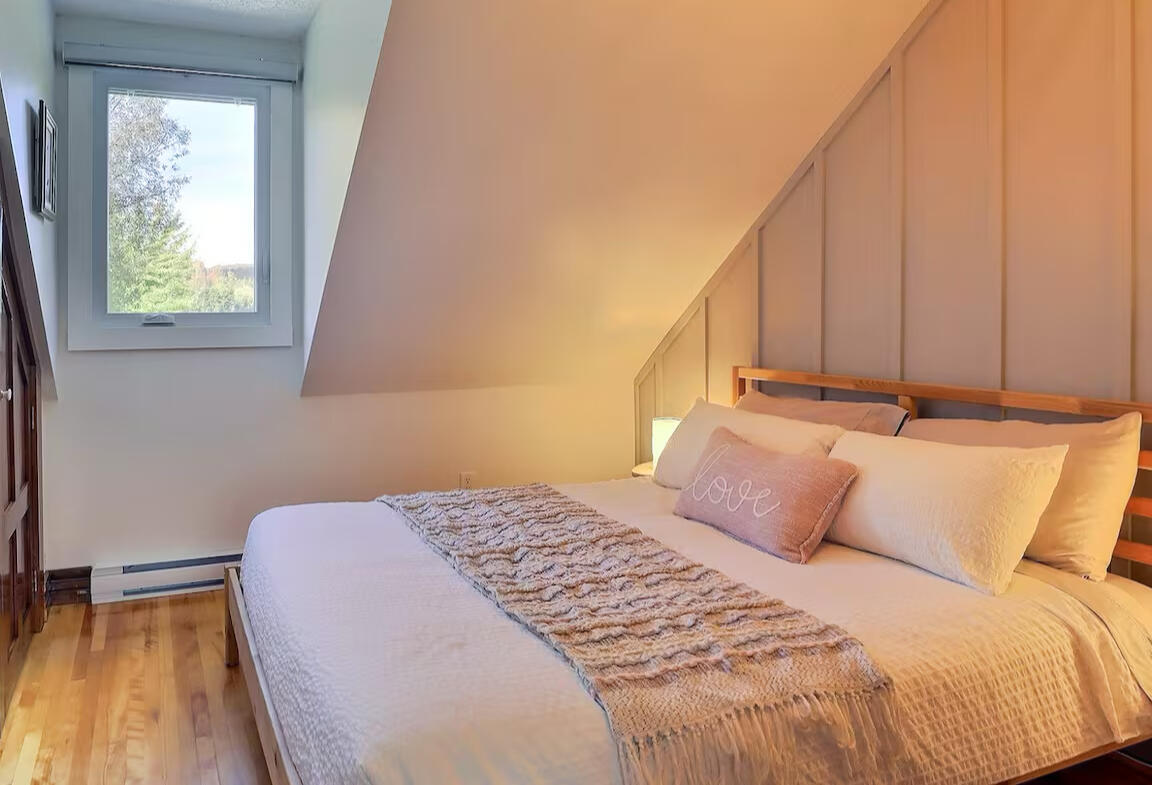 Chambre lumineuse du chalet Le Monarque près de Magog avec lit double et ambiance chaleureuse Chambre confortable du chalet Le Monarque près de Magog en Estrie avec lit double et vue sur le lac lovering