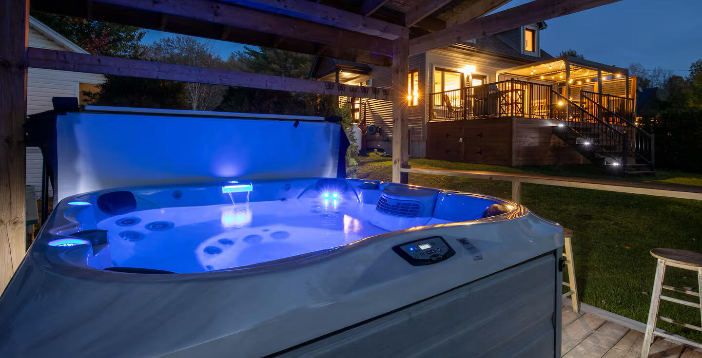 Spa privé du chalet à louer Le Monarque près de Magog en Estrie Spa extérieur du chalet Le Monarque près de Magog en Estrie avec vue sur le chalet illuminé le soir