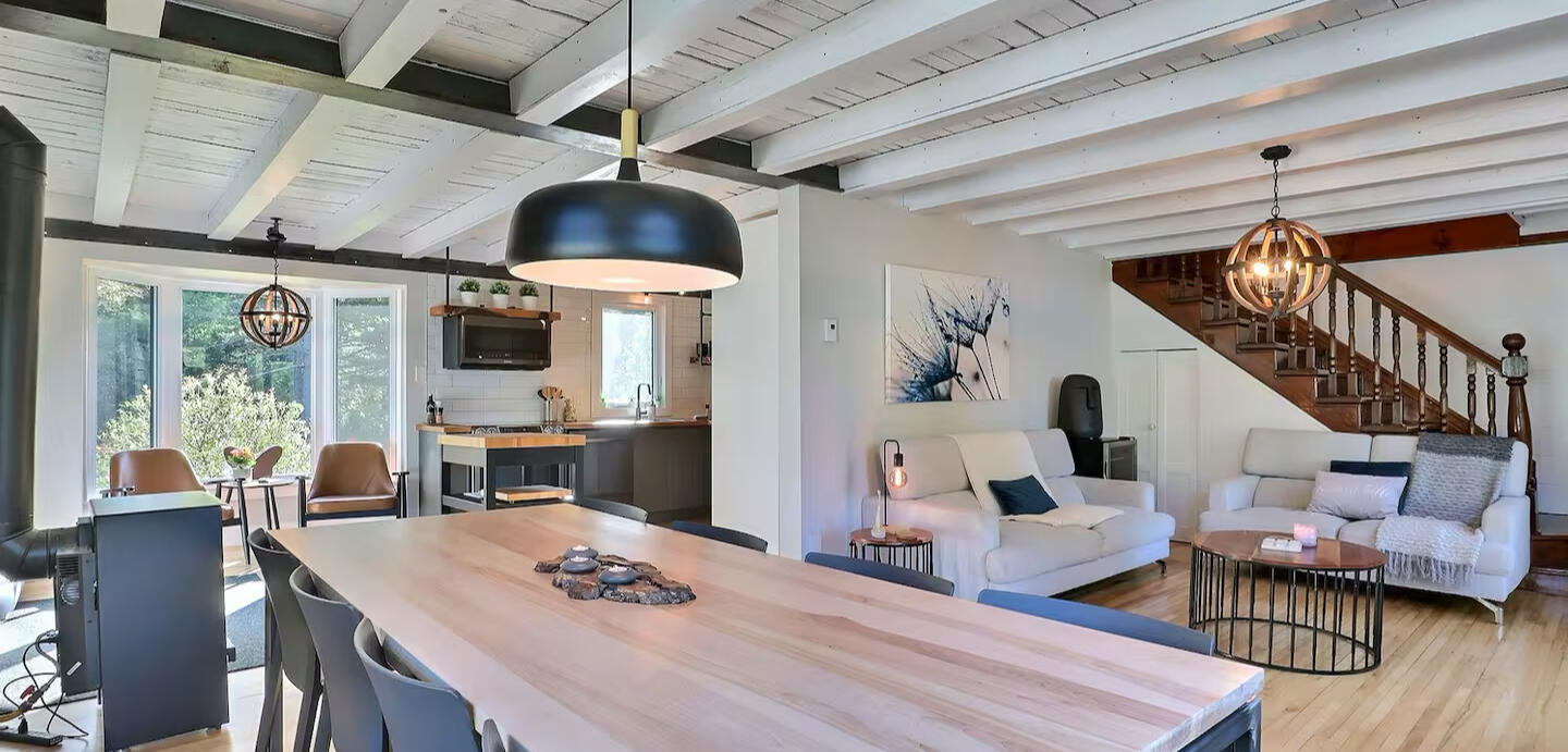 Salon et salle à manger lumineux du chalet Le Monarque près de Magog avec cuisine ouverte et grande table en bois pour 8 personnes
